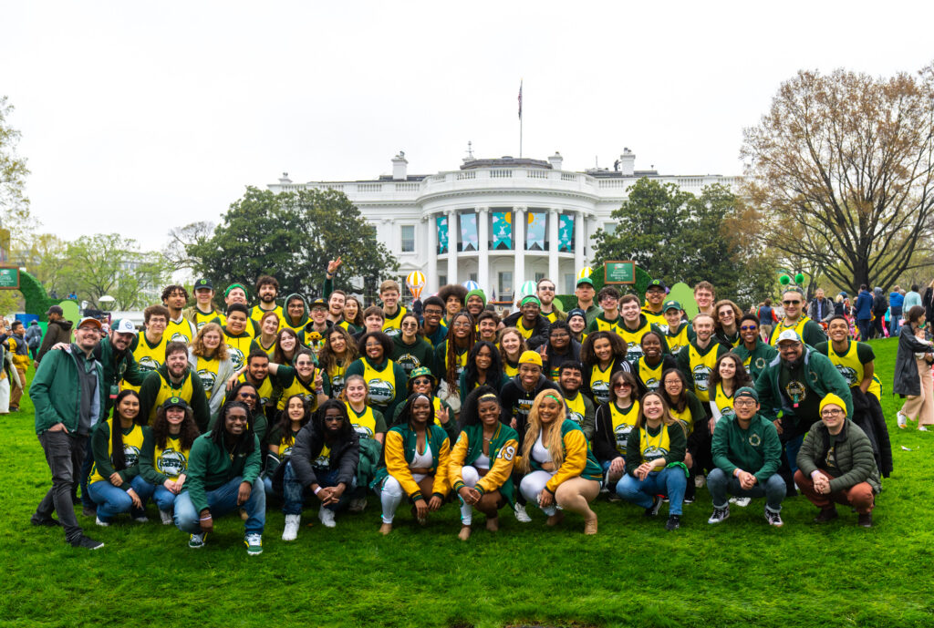 The Green Machine stands on the south lawn in front of the White House in Washington, DC on an overcast day for a group photo. The band is wearing yellow jerseys with green accents.