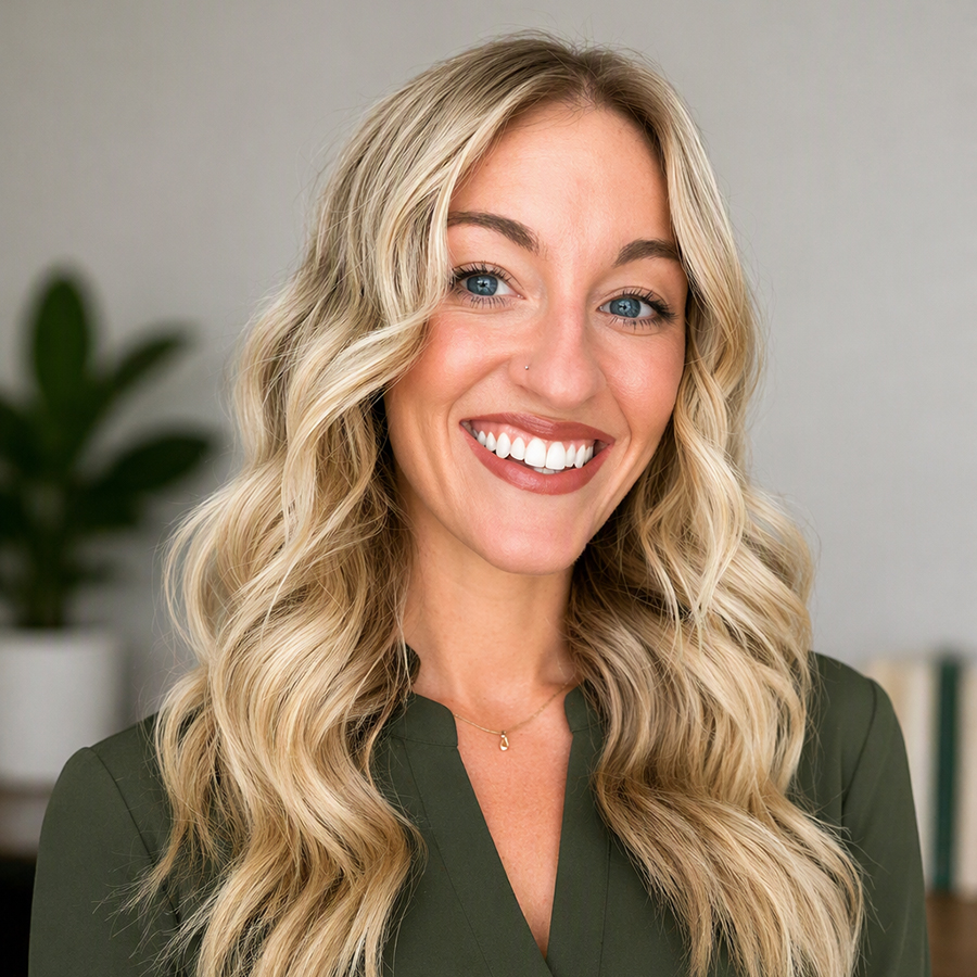 Shelby is smiling and seated in her office. She is wearing a green blouse. There is a potted plant behind her to her right.