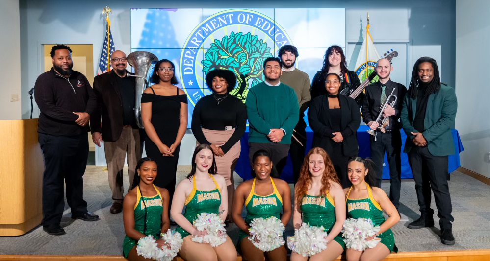 Members of Green and Gold Soul pose with Doc Nix, Mason cheerleaders, and Department of Education officials in front of the department of education seal.