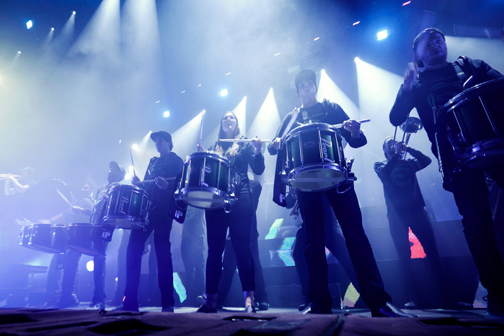 The spirit drumline performs on stage at the anthem in blue-white spotlights with Griz. The picture is close up to the stage looking up at the band.