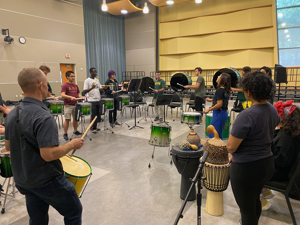 Spirit drumline students and Shane Nickels stand with guest artists in the Performing Arts Building room 3001 as they perform with their drums.