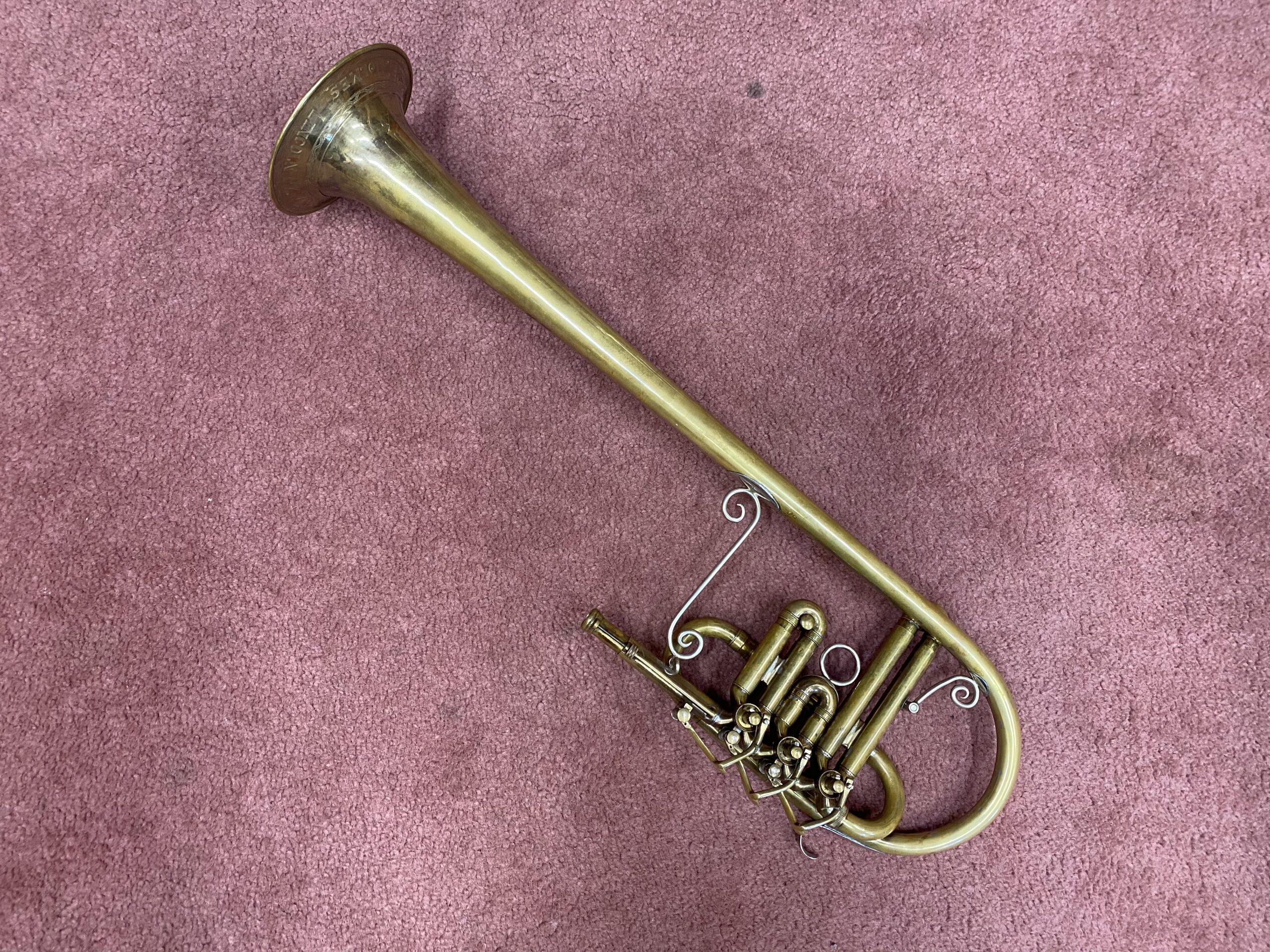 A reproduction Bb cornet featuring an over-the-shoulder bell design. The instrument rests on a pink carpet.