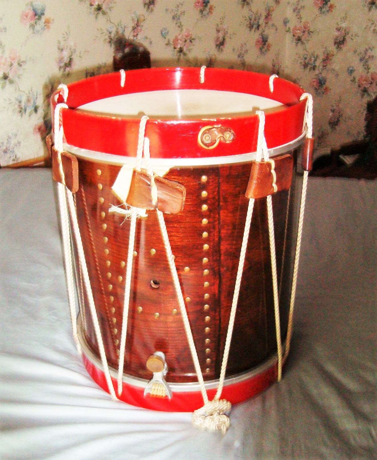 A brown wood rope drum with red hoops, brown leather ears, and a tack design on the shell