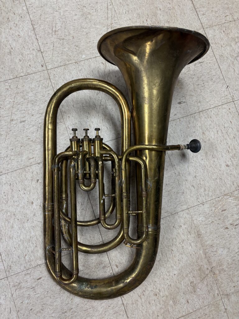 A brass Eb tuba with three piston valves laying on a dirty white tile floor